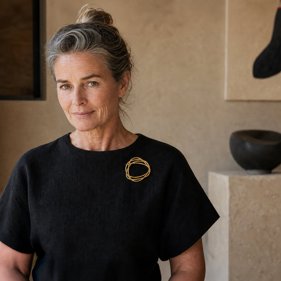 Woman wearing the matt-gold inSync Rings Brooch in a warm contemporary gallery interior.
