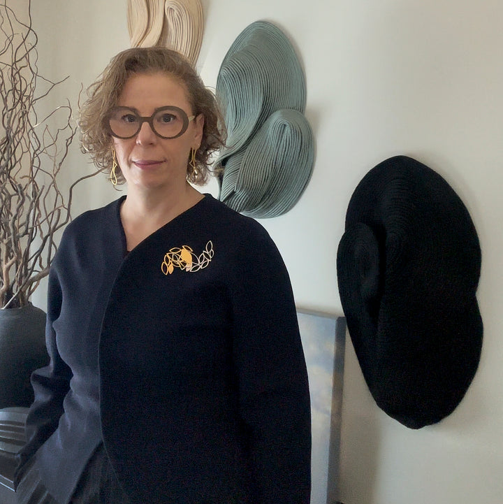 Iris Saar Isaacs wearing the X2 Stillness Raw and Gold brooches layered on a navy knit.